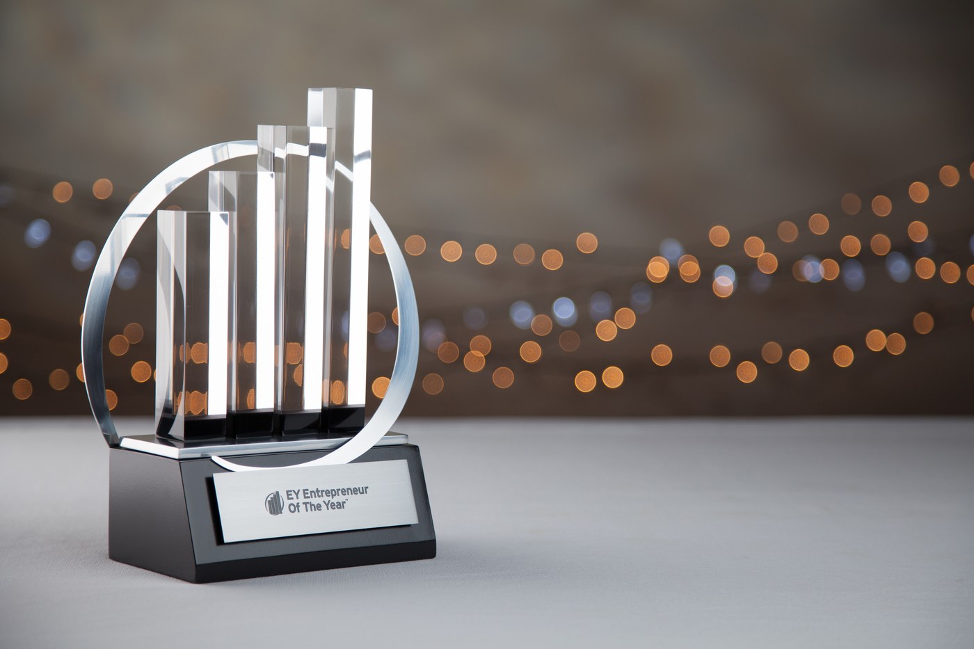 An Ernst & Young Entrepreneur of the Year crystal trophy on a black plinth, against a bokeh-lit backdrop.