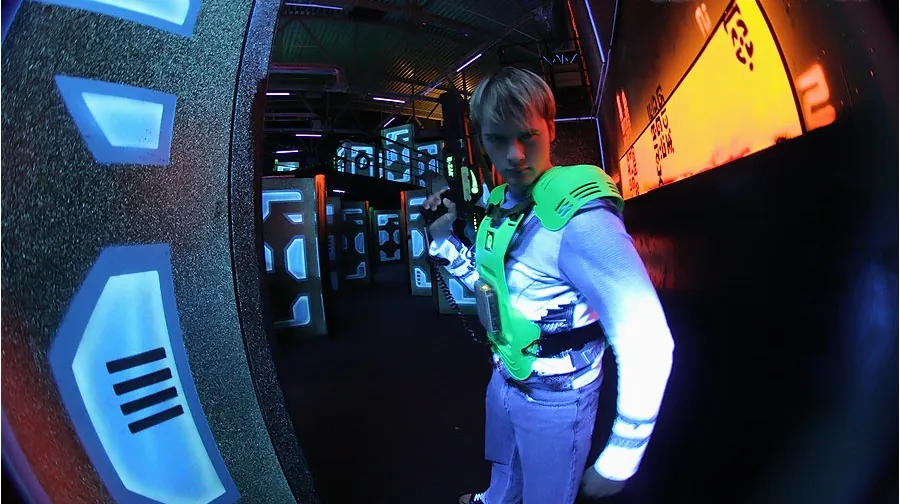 A Q-Zar laser-tag arena in operation, with a young player in vest and phaser, surrounded by the neon-and-black arena environment.