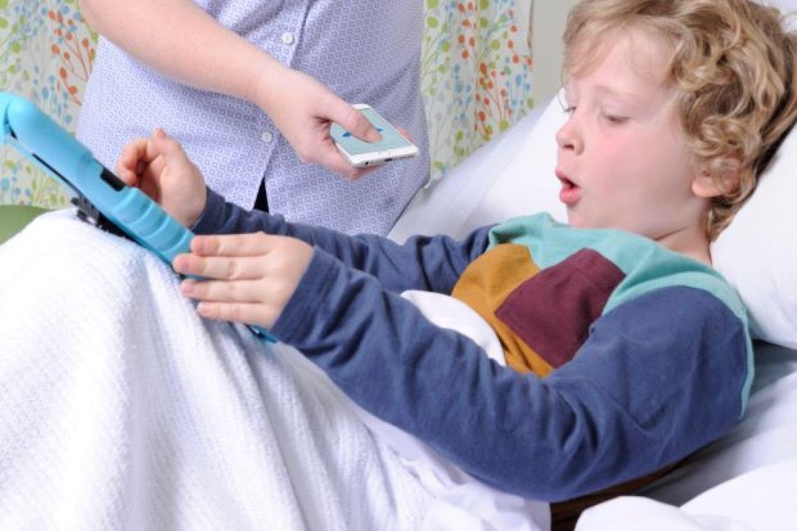 A young patient in a hospital bed coughs while a clinician records the cough on a smartphone running ResAppDx.
