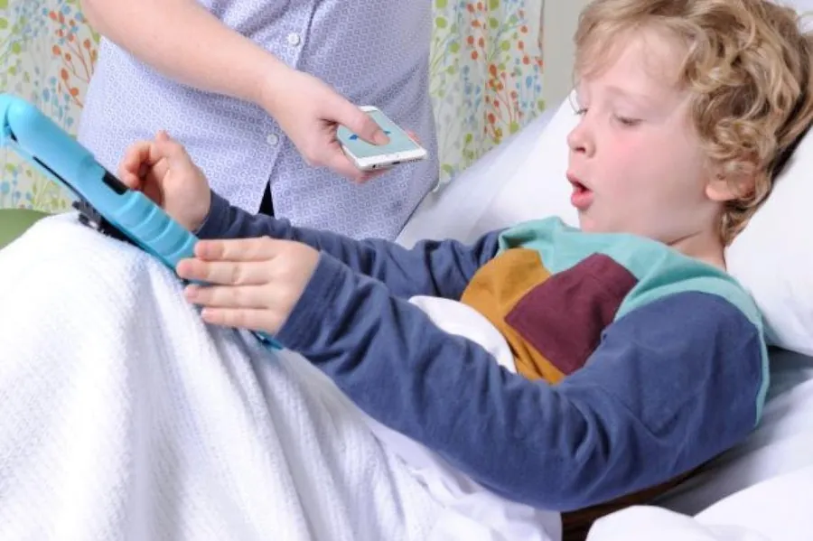 A young patient in a hospital bed coughs while a clinician records the cough on a smartphone running ResAppDx.