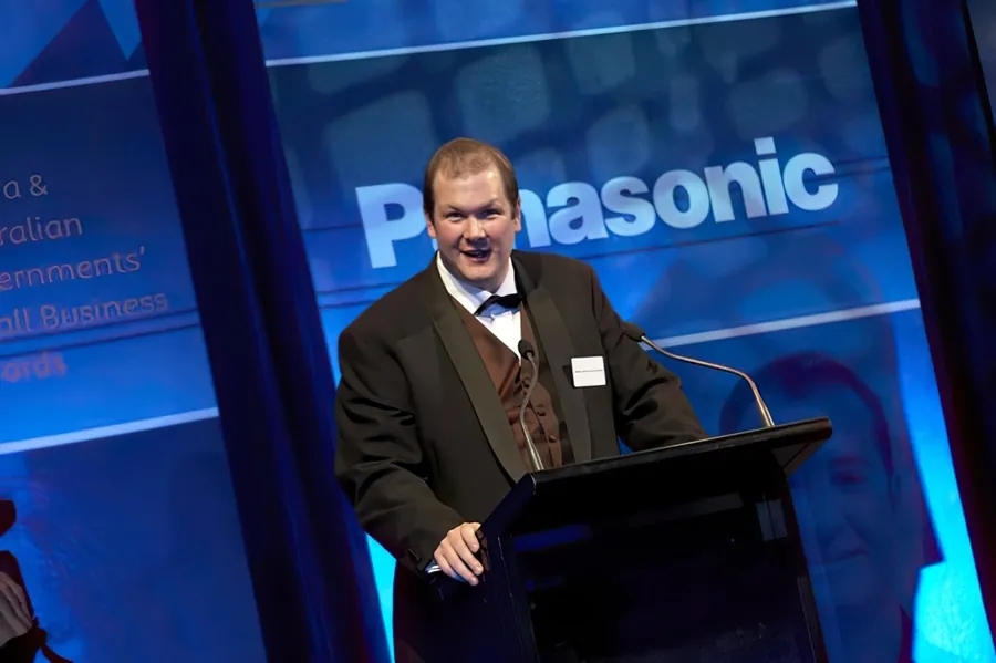 Nathan Buzza accepting the WA Medium Business award at the 2005 Telstra Business Awards ceremony — Panasonic-sponsored stage backdrop.